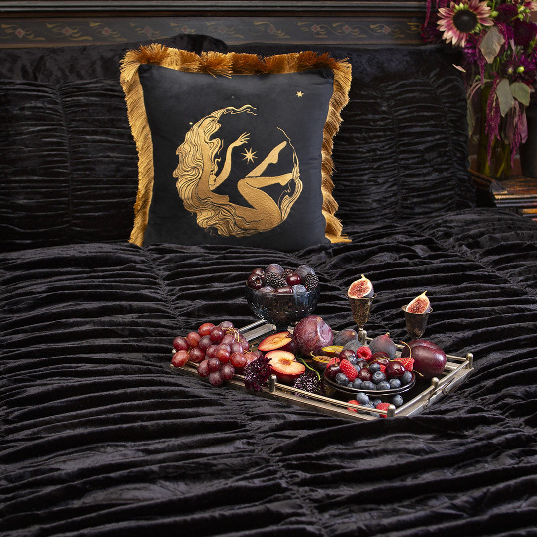 Black scalloped velvet bedding with a gold and black embroidered throw pillow on a bed. 
