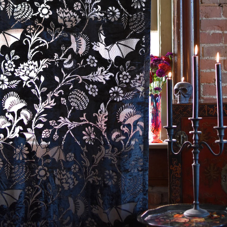 Black velvet curtain with gothic bat and botanical motifs hanging in a room with a window.