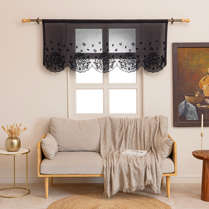 Black cotton window valance and curtains with black spider web cottagecore and whimsigoth embroidery. It is hung up on a curtain rod above a couch in a living room.