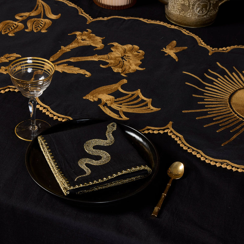 Bronze Embroidered Table Runner featuring motifs from Sin in Linen's Night Garden pattern. Make a dark, witchy table with this centerpiece. Also featured is the gold Embroidered Snake Sapkin. 