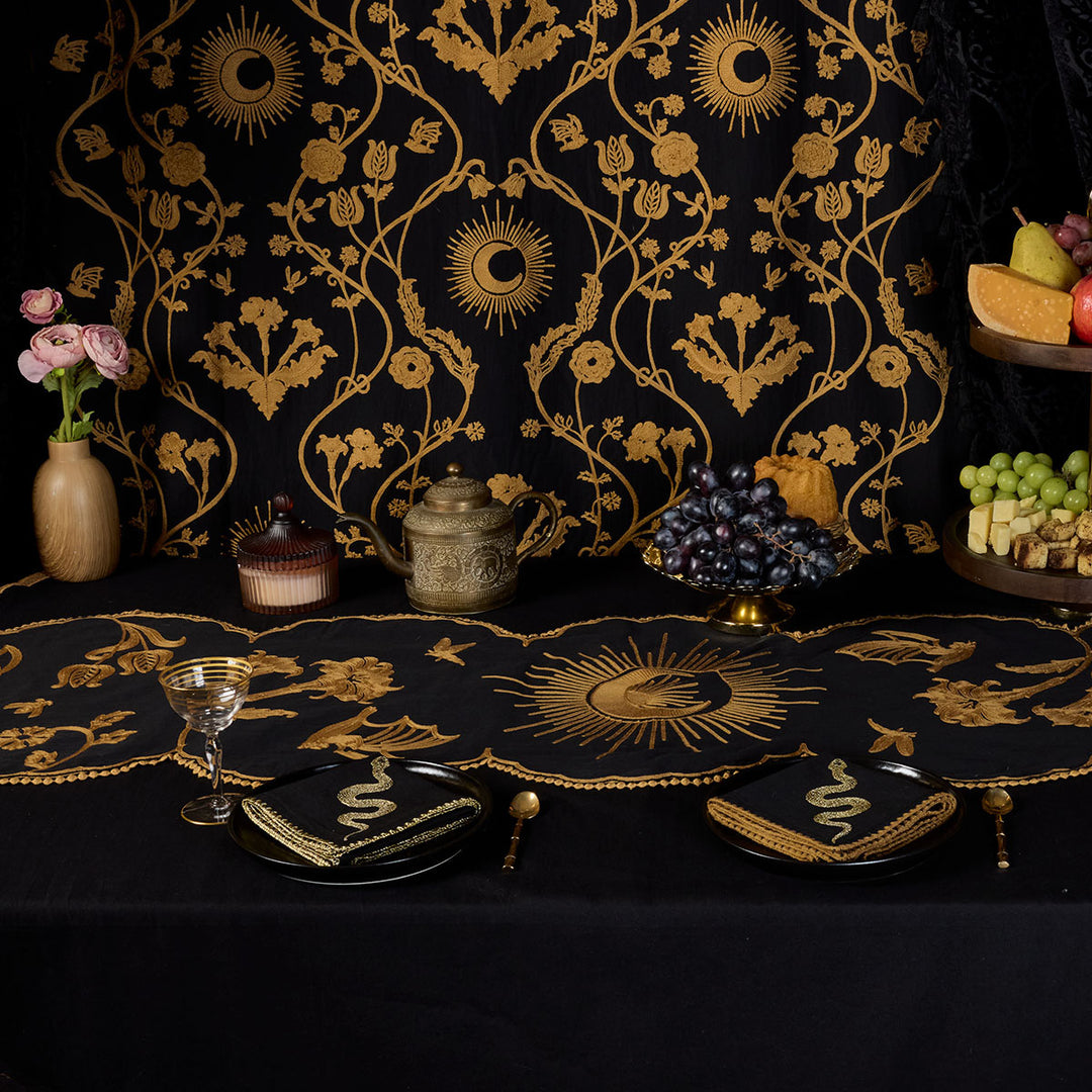 A grand witchy tablescape with Sin in Linen's Embroidered Night Garden Table Linens collection. Bronze embroidered moons and dark florals on a black backdrop. 