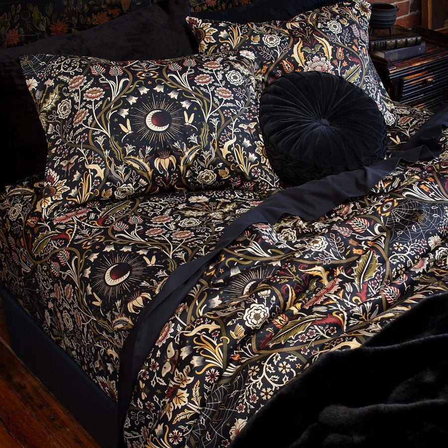 Night Garden Harvest botanical bedding on a bed. Features florals, serpents, and spiders for a nature inspired bedroom. Accented with velvet pillowcases and throw pillow. 