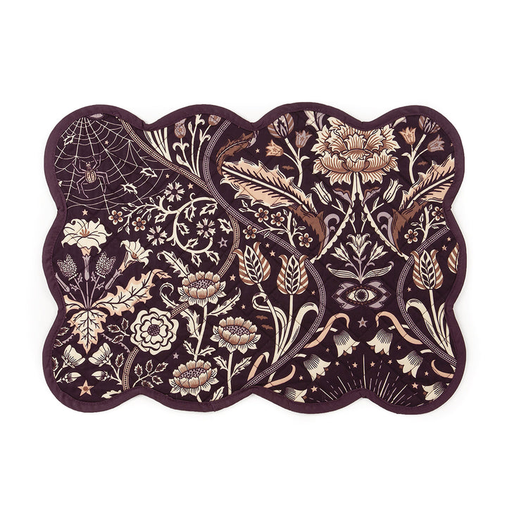 A dark floral quilted placemat with a purple background and scalloped edges