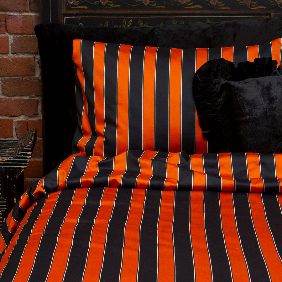 Pumpkin orange and black striped pillowcases on a bed. Vintage circus inspired bedding. 