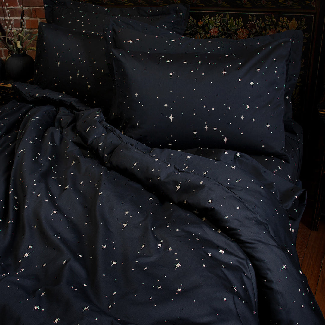 Celestial and night sky inspired bedding featuring bronze stars by Sin in Linen. On the bed is a coordinating bed set.