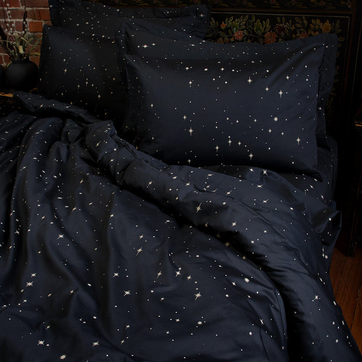 Celestial and night sky inspired bedding featuring bronze stars by Sin in Linen. On the bed is a coordinating bed set.