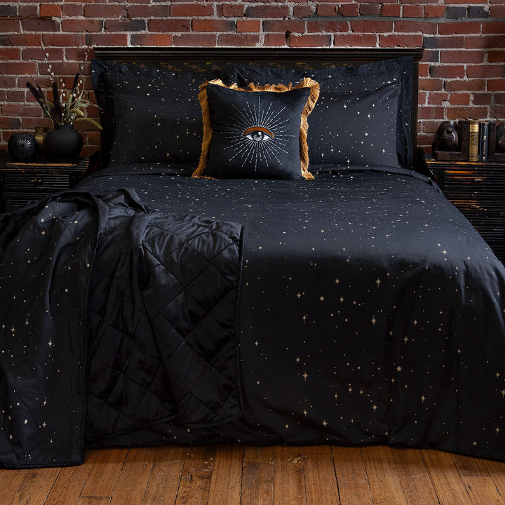 Celestial and night sky inspired bedding featuring bronze stars by Sin in Linen. On the bed is a bed set, velvet blanket, and velvet throw pillow with an eye design. 