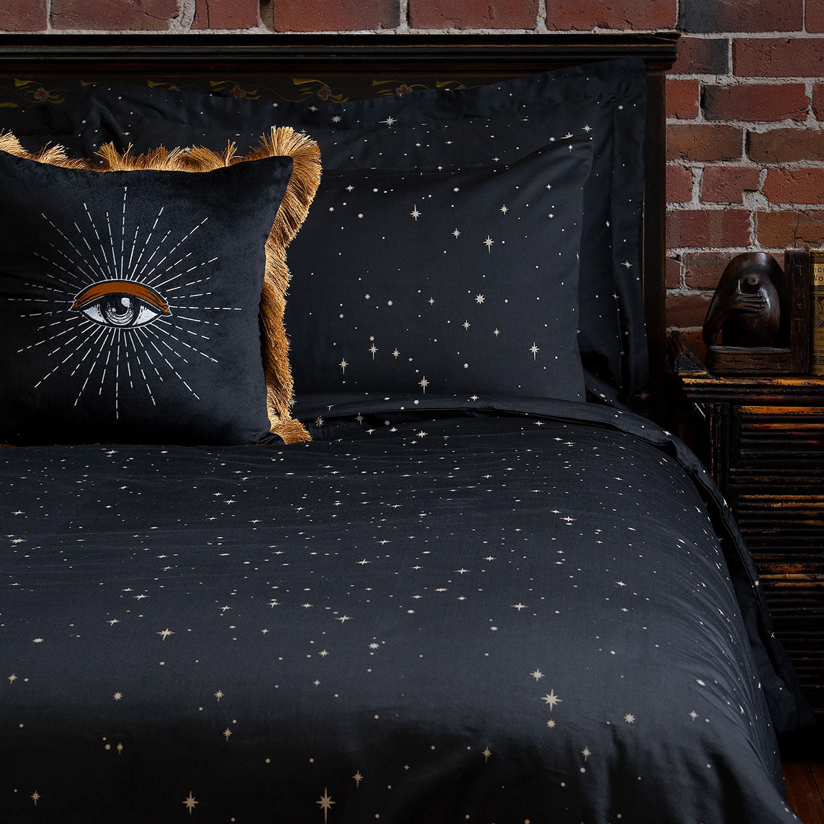 Celestial and night sky inspired bedding featuring bronze stars by Sin in Linen. On the bed is a coordinating bed set with an embroidered velvet throw pillow.