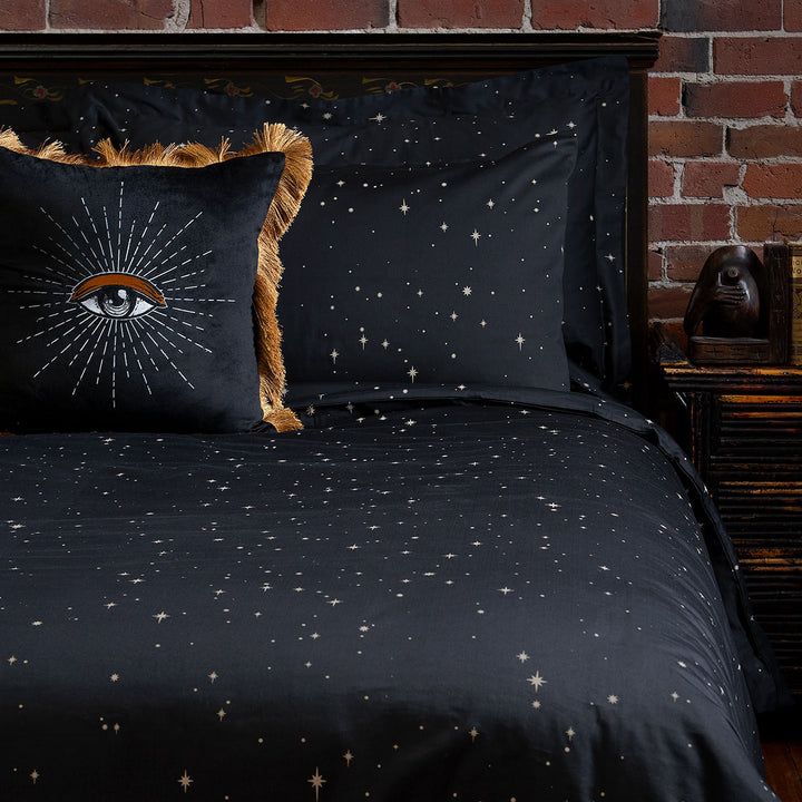 Celestial and night sky inspired bedding featuring bronze stars by Sin in Linen. On the bed is a coordinating bed set with an embroidered velvet throw pillow.