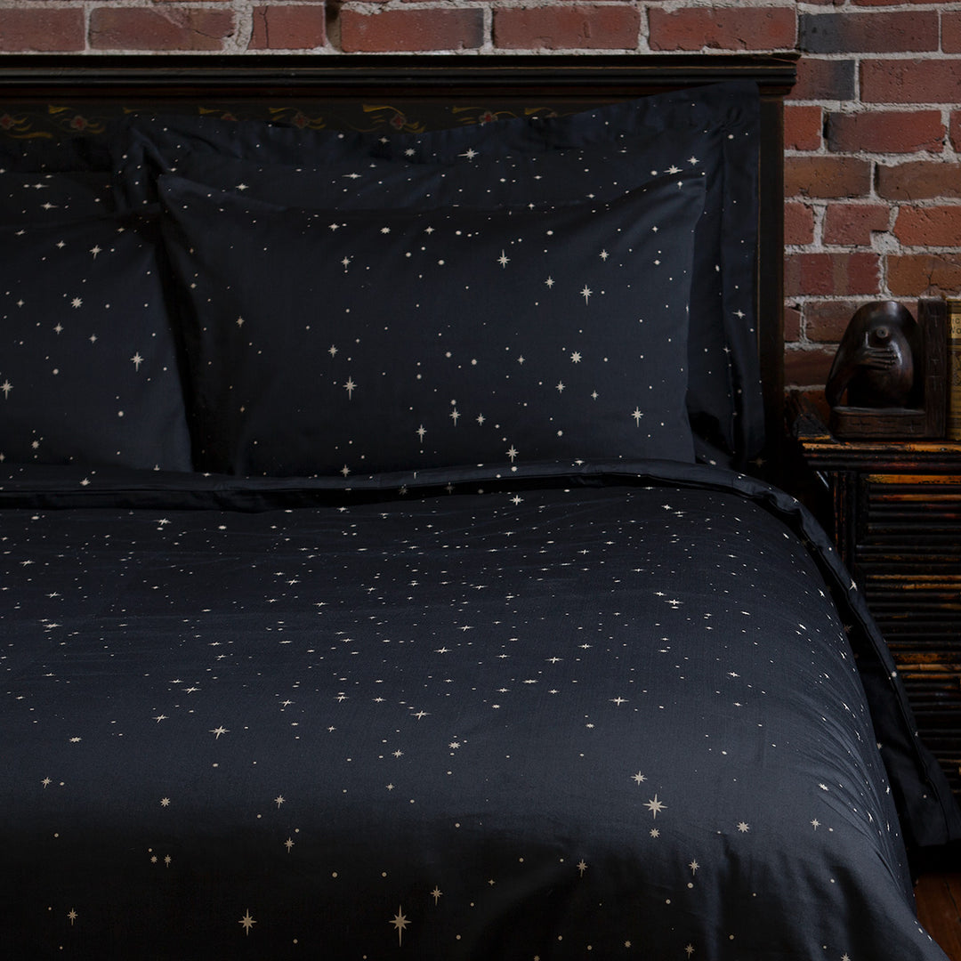 Celestial and night sky inspired bedding featuring bronze stars by Sin in Linen. On the bed is a coordinating bed set.
