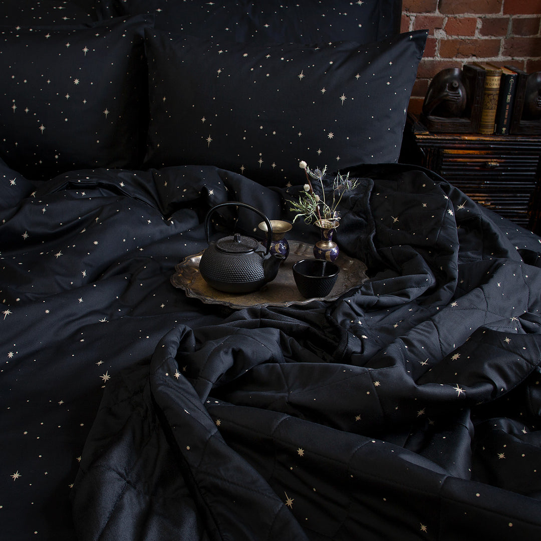 Celestial and night sky inspired bedding featuring bronze stars by Sin in Linen. On the bed is a coordinating bed set. 