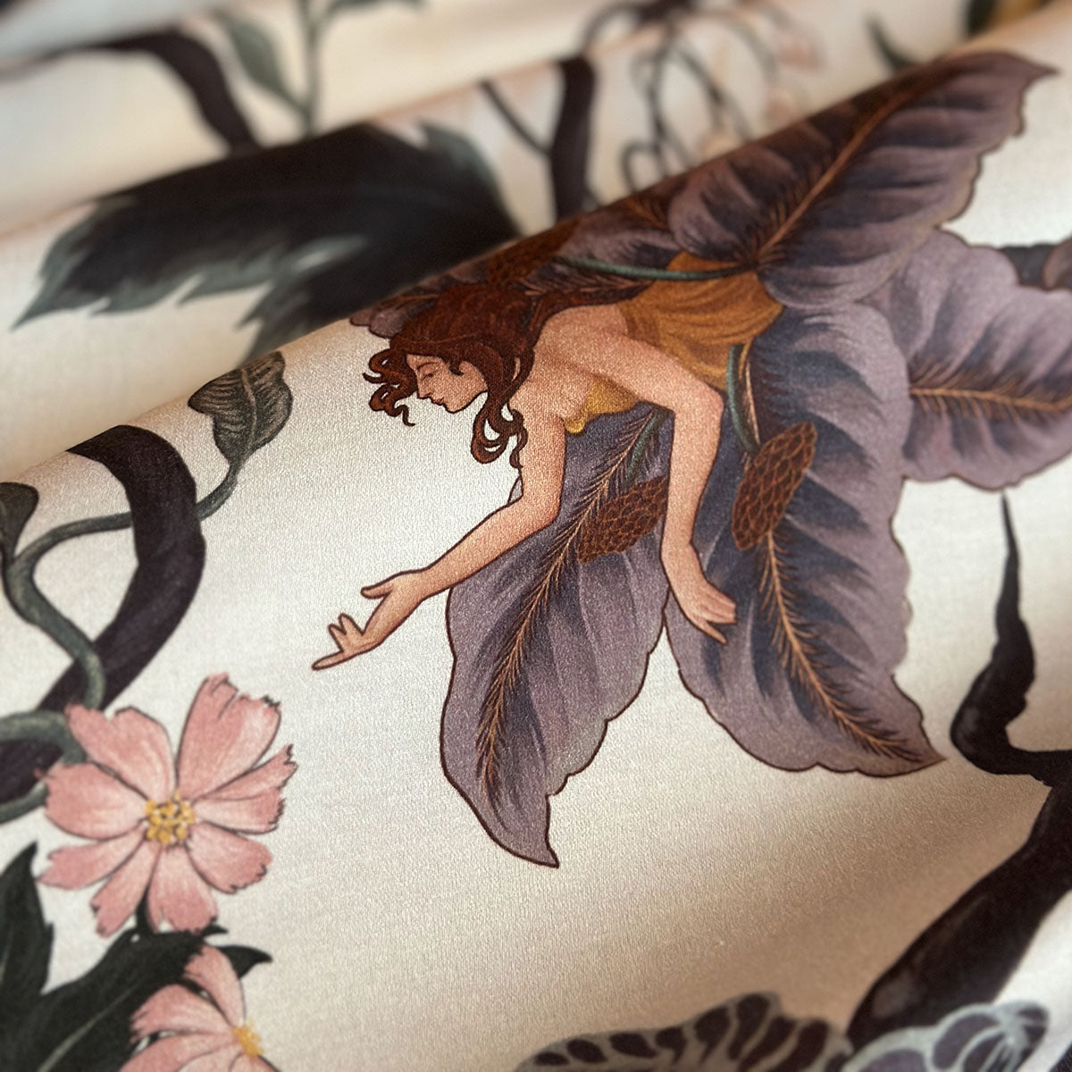 Swatch of fabric featuring nymphs blooming out of flowers on a light botanical background. Fairy inspired bedding decor by Sin in Linen with hues of lilac and rose. 
