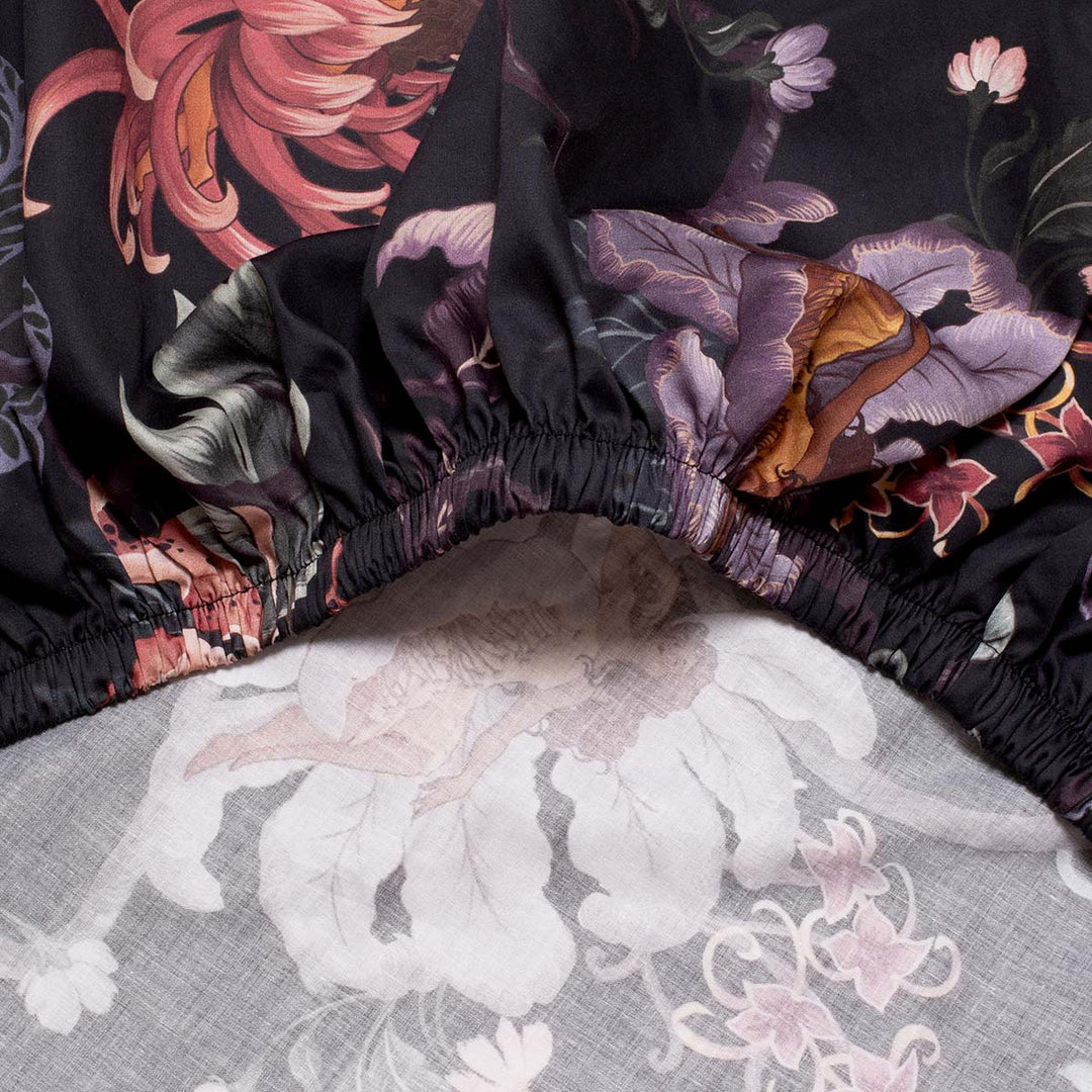 Romantic floral bedding by Sin in Linen. Nymphs bloom out of flowers on a dark background on these fairy inspired sheets. Hues of lilac and rose abound. 
