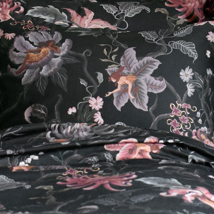 Swatch of fabric featuring nymphs blooming out of flowers on a dark botanical background. Fairy inspired bedding decor by Sin in Linen with hues of lilac and rose. 