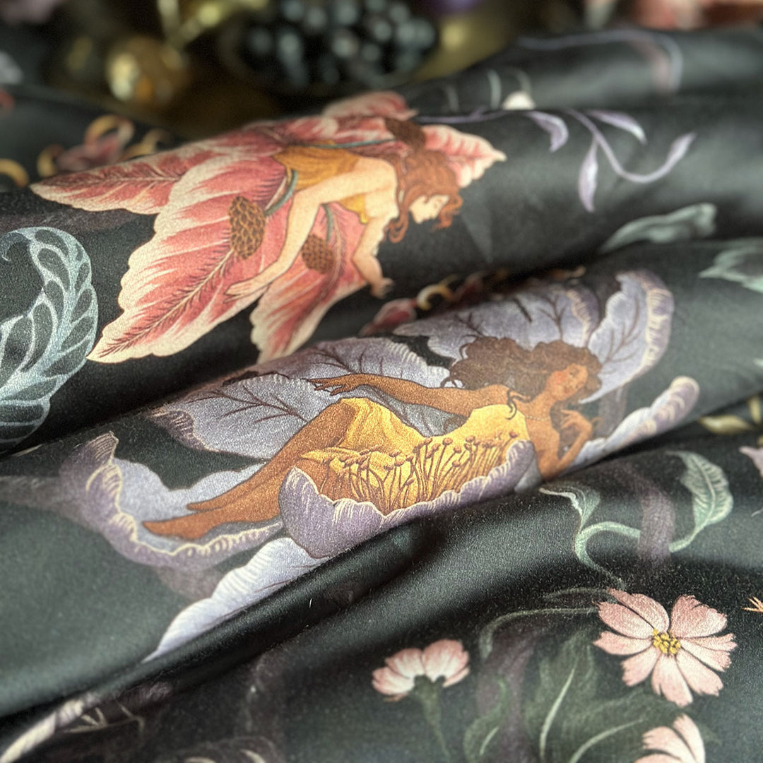 Swatch of fabric featuring nymphs blooming out of flowers on a dark botanical background. Fairy inspired bedding decor by Sin in Linen with hues of lilac and rose. 