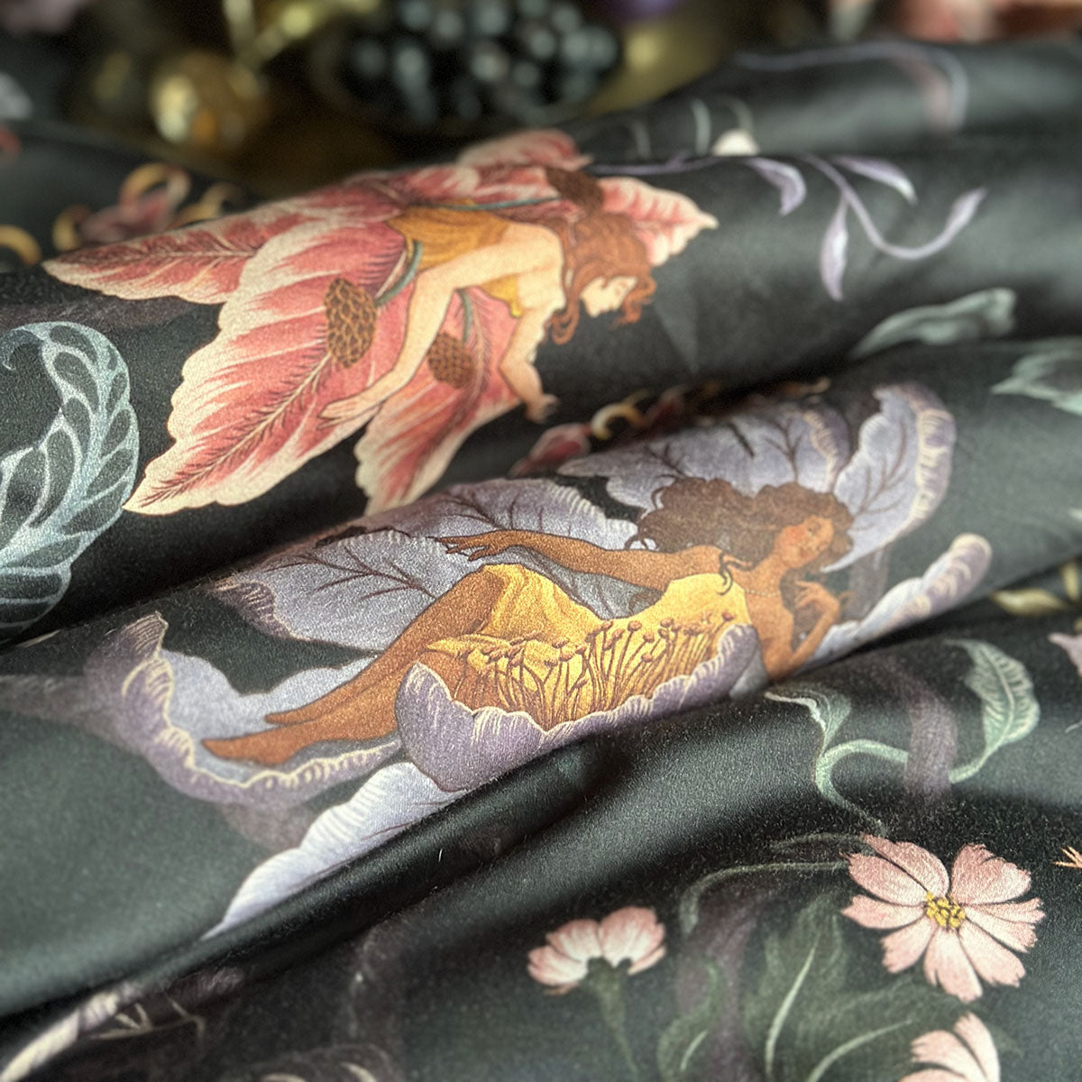 Swatch of fabric featuring nymphs blooming out of flowers on a dark botanical background. Fairy inspired bedding decor by Sin in Linen with hues of lilac and rose. 