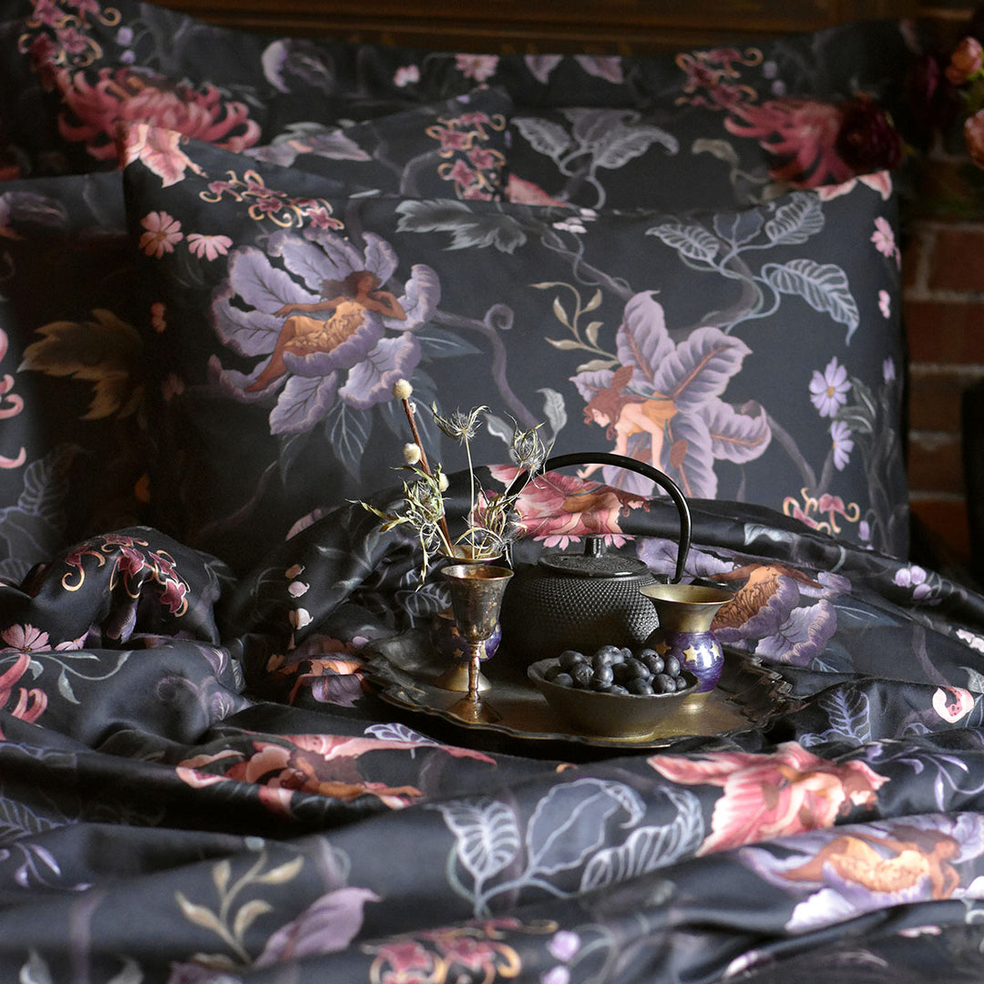 Romantic floral bedding by Sin in Linen. Nymphs bloom out of flowers on a dark background in this fairy inspired bedding collection. Hues of lilac and rose abound. 