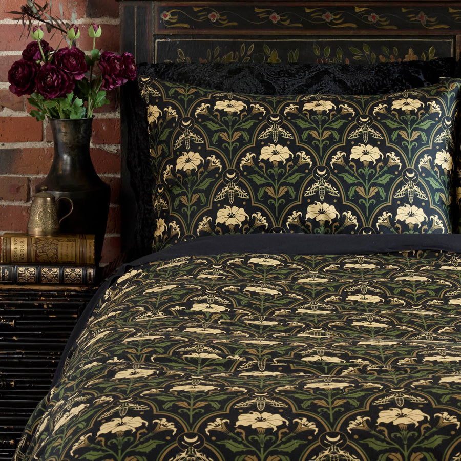 Sin in Linen's Datura Deco print pillowcases and shams on a bed. Inspired by art deco accents and gothic botanical motifs, Datura Deco features moths, crescent moons, and blooming florals. 