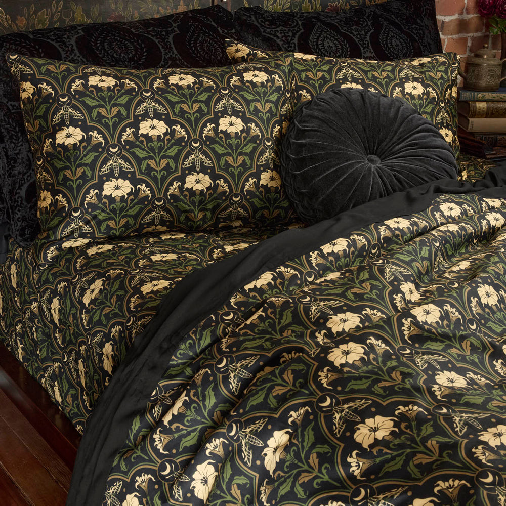 Sin in Linen's Datura Deco print bedding on a bed. Inspired by art deco accents and gothic botanical motifs, Datura Deco features moths, crescent moons, and blooming florals. Vintage inspired pillows dress the bed. 
