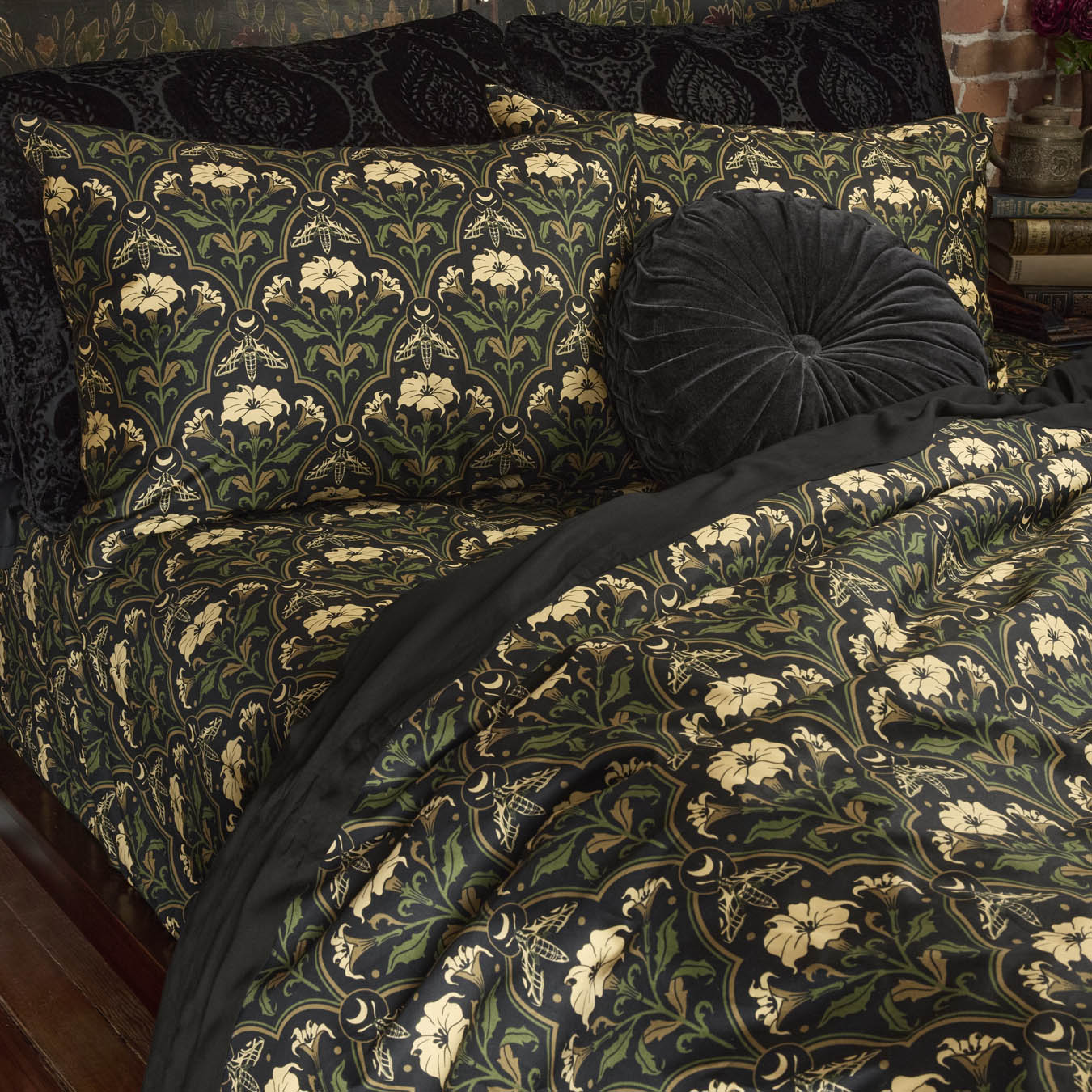 Sin in Linen's Datura Deco print bedding on a bed. Inspired by art deco accents and gothic botanical motifs, Datura Deco features moths, crescent moons, and blooming florals. Vintage inspired pillows dress the bed. 