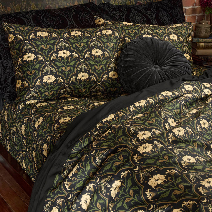Sin in Linen's Datura Deco print bedding on a bed. Inspired by art deco accents and gothic botanical motifs, Datura Deco features moths, crescent moons, and blooming florals. Vintage inspired pillows dress the bed. 