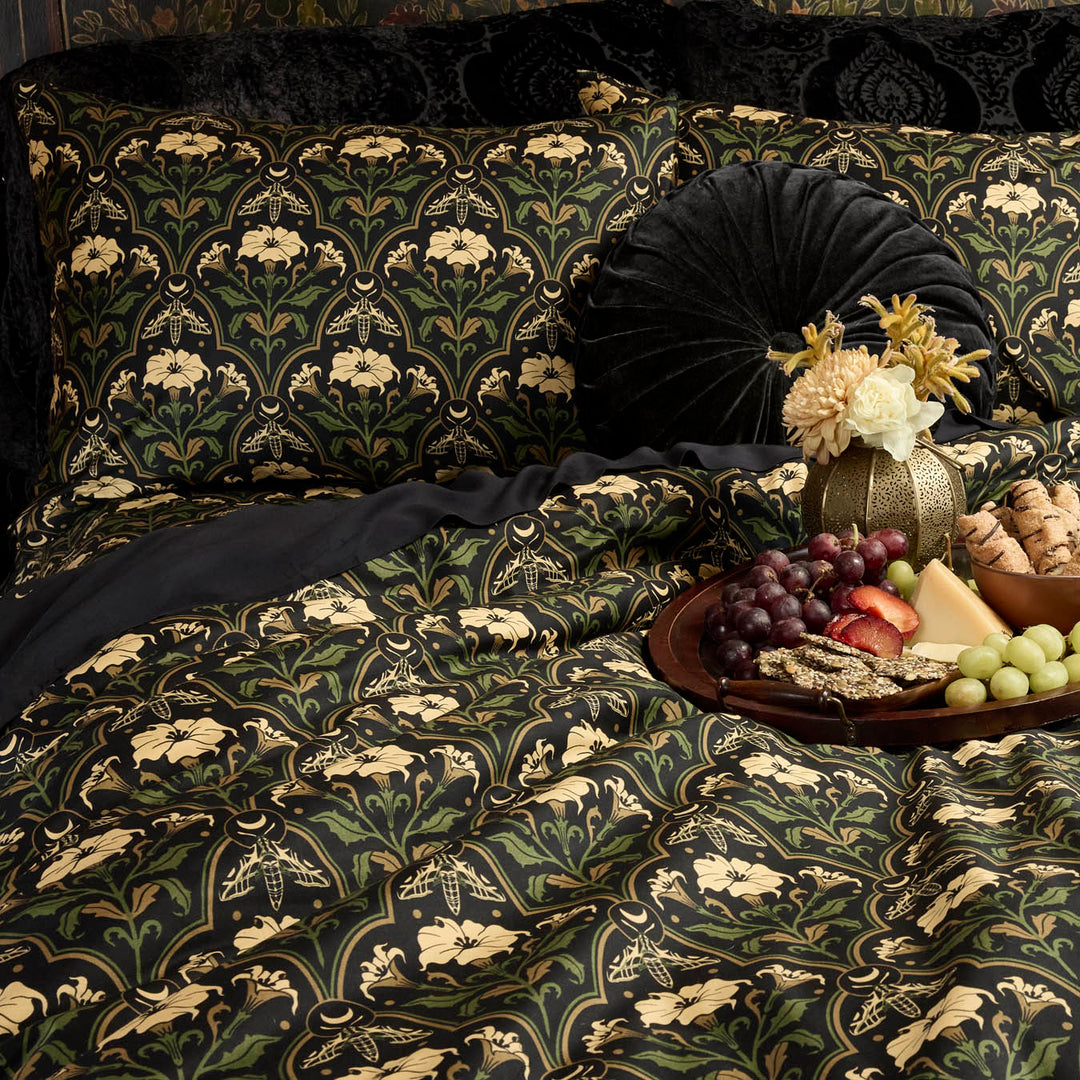 Gothic Botanical Art Deco Bedding with the Datura Deco print featuring moths, gilded accents, and blooming florals. Velvet accents dress the bed as well.