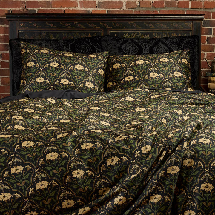 Sin in Linen's Datura Deco bedding on a bed. Inspired by art deco accents and gothic botanical motifs, Datura Deco features moths, crescent moons, and blooming florals. 