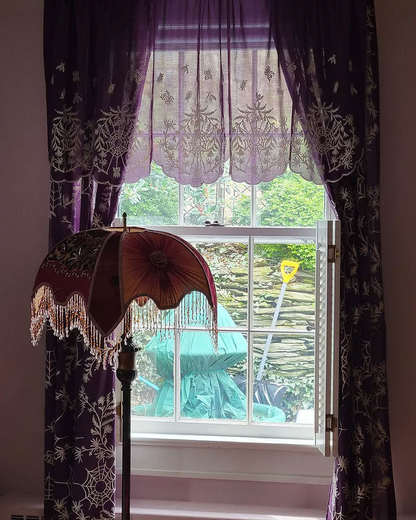 Purple and Ivory Spider Web Lace curtains hung on a window with a lamp
