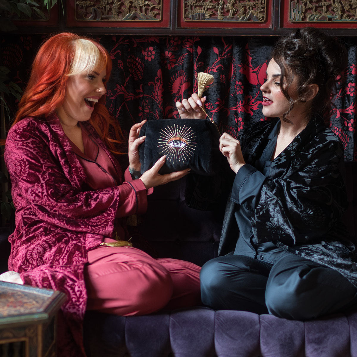 Two women with a velvet makeup bag with an embroidered mystical eye. Wearing bamboo and velvet sleepwear from Sin in Linen.