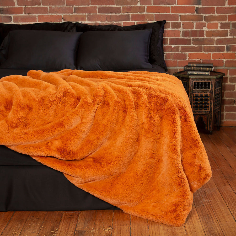 Pumpkin orange faux fur blanket on a bed. Luxury Halloween decor. 