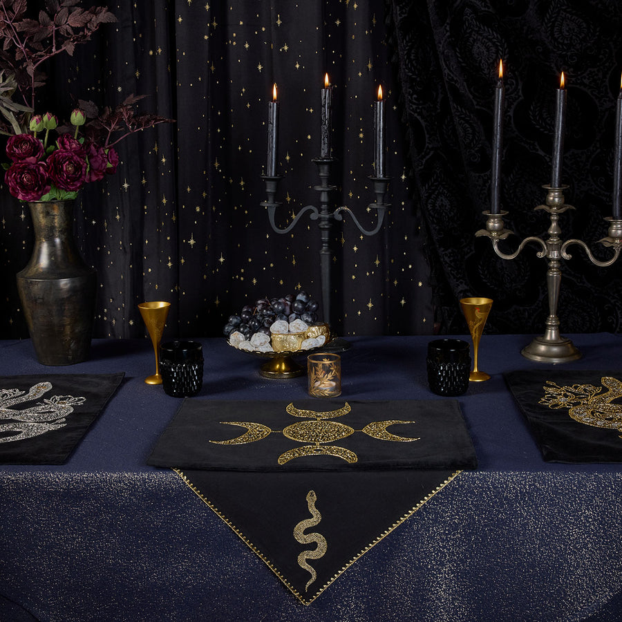 A ritualcore inspired witchy tablescape from Sin in Linen. Navy Lurex Tablecloths with gold glitter sit below beaded altar cloths and embroidered napkins for a gilded feast. 
