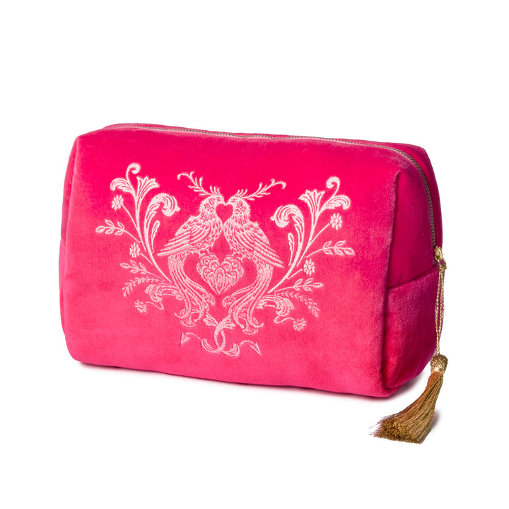 Pink velvet toiletry bag with embroidered love birds and a gold tassel on a white background