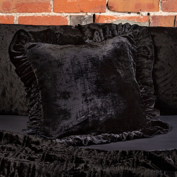 Black velvet throw pillow with a ruffled edge on a bed. 
