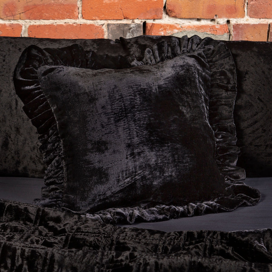 Black velvet throw pillow with a ruffled edge on a bed. 