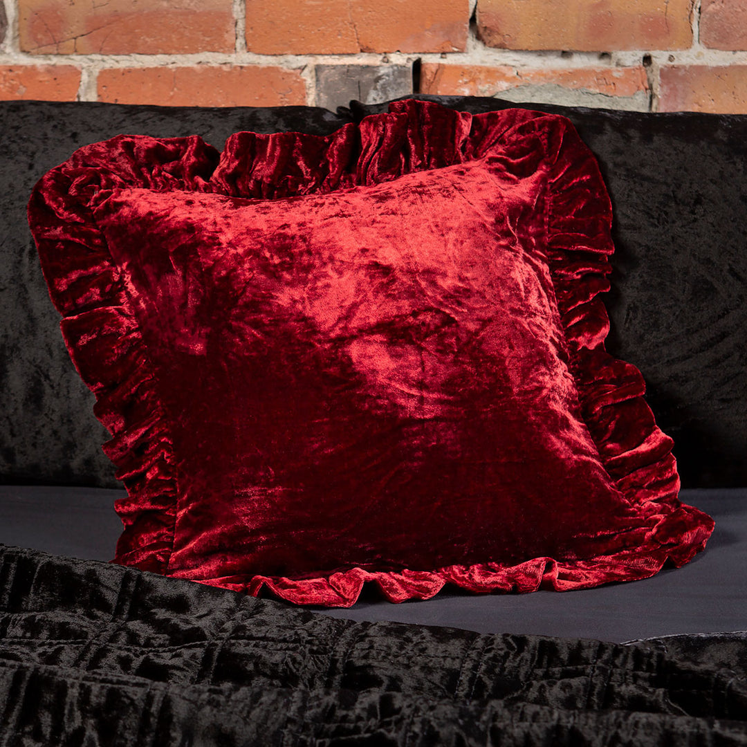 Ruby red velvet throw pillow with a ruffled edge on a bed. 