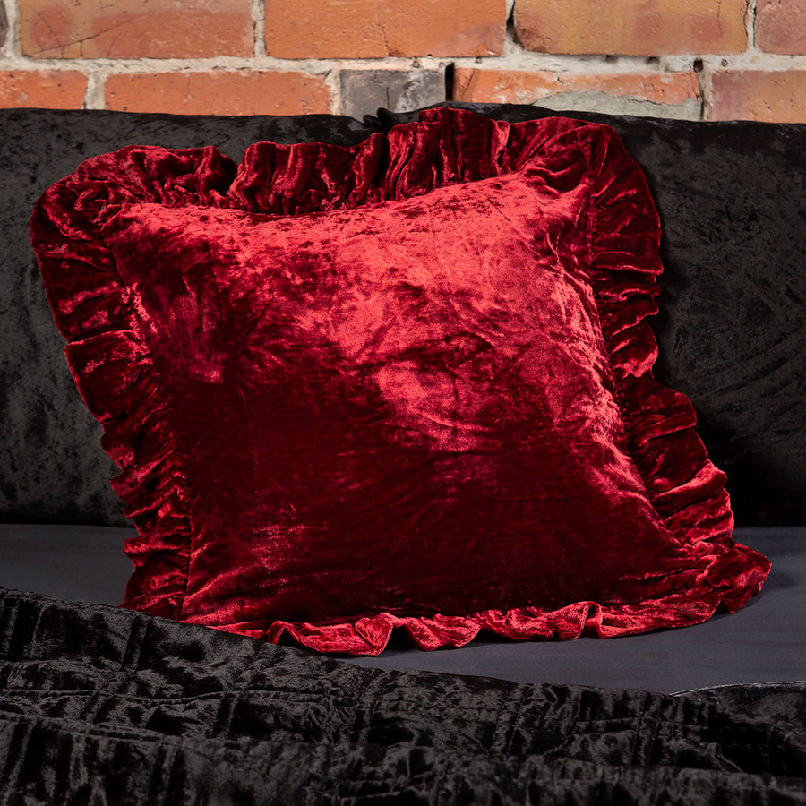 Ruby red velvet throw pillow with a ruffled edge on a bed. 