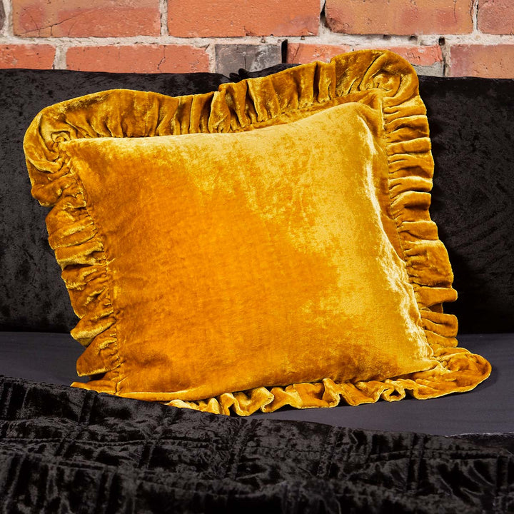 Gold velvet throw pillow with ruffled edges on a bed. 