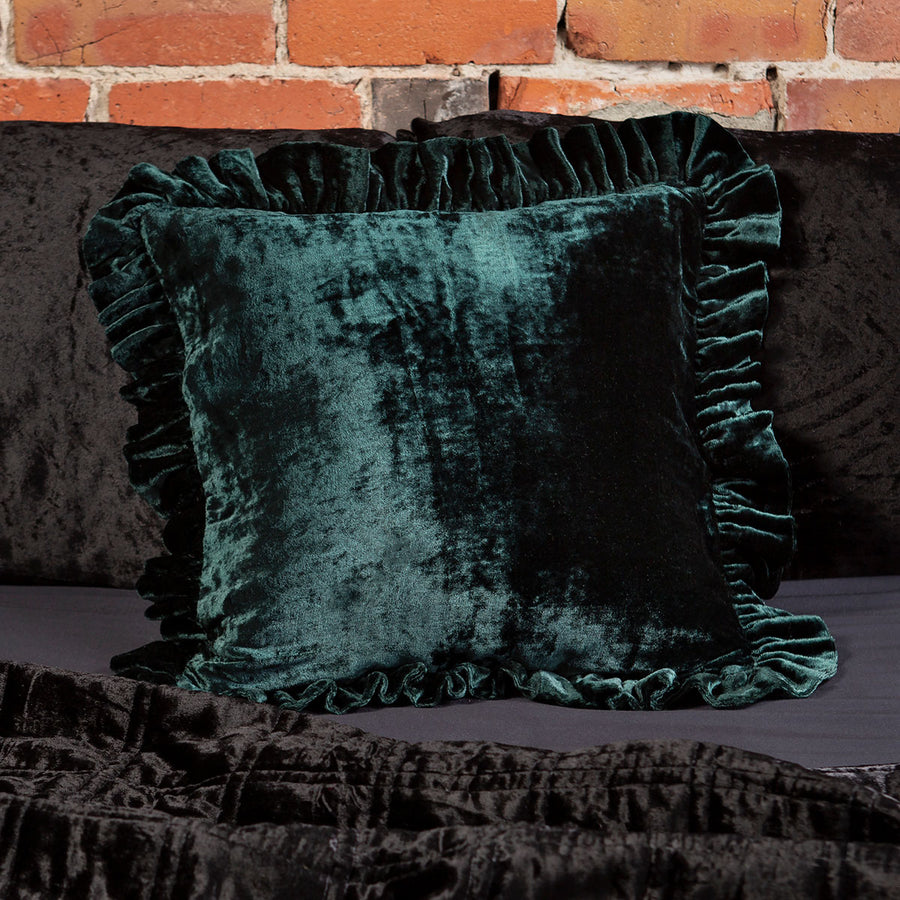 Forest Green velvet throw pillow with a ruffled edge on a bed. 