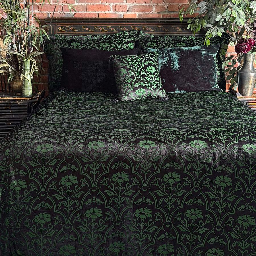 Sin in Linen's Velvet Datura bedding collection on a bed with coordinating velvet pillowcases. Green gothic botanical pattern featuring datura blooms and bats in a flocked velvet design. Dark, witchy decor. 