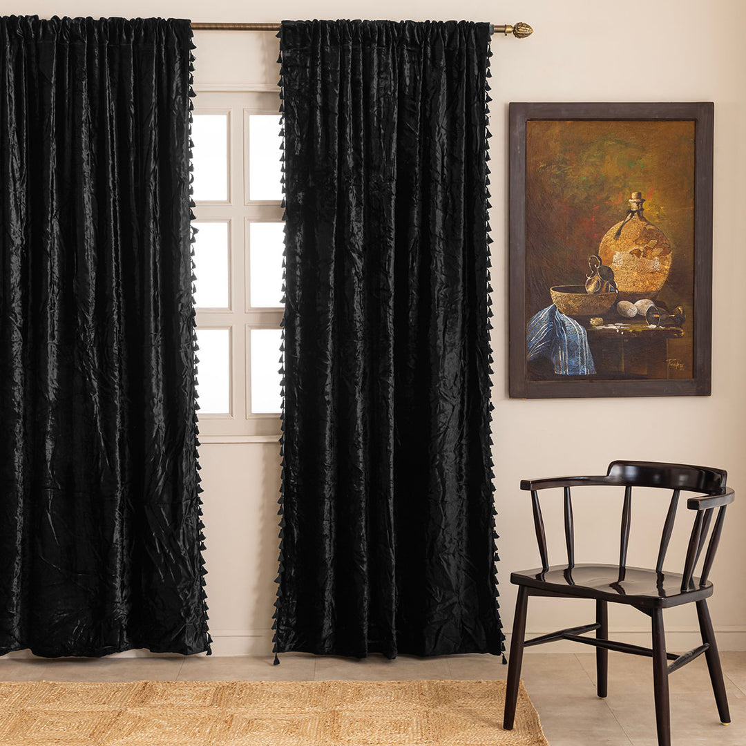 Black velvet curtains with tassels in a room with a chair and a painting on the wall.