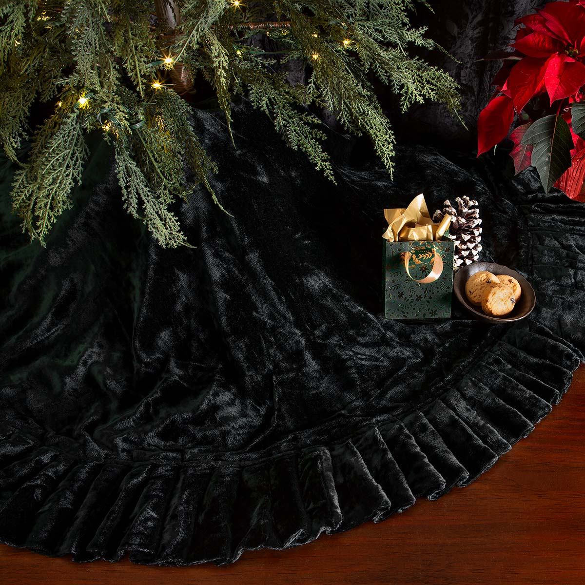 Black velvet tree skirt with a gift and poinsettia under a decorated Christmas tree.