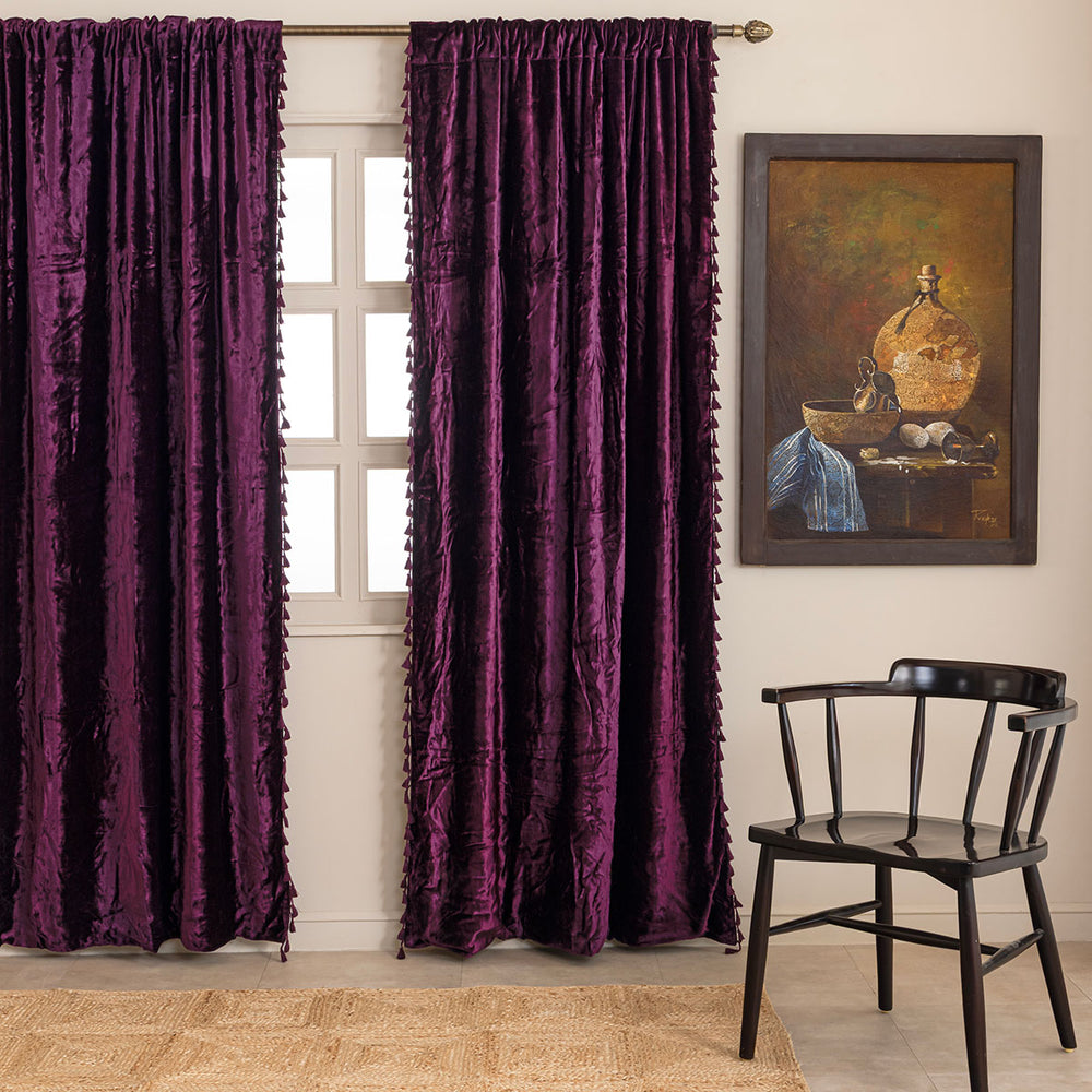 Purple velvet curtains with tassels in a room with a painting and a chair.