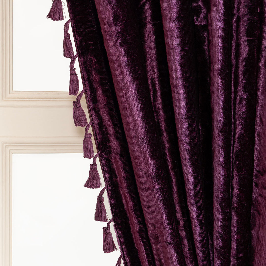 Close-up of a purple velvet curtain with tassels in front of a window.