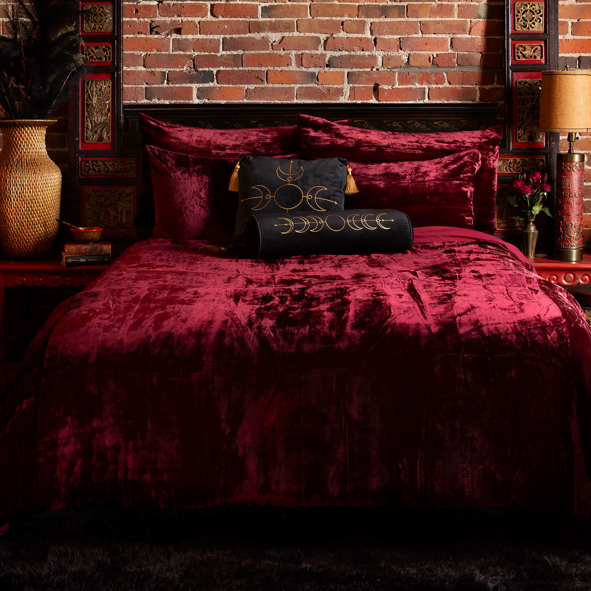 A ruby velvet duvet cover set on a bed, with matching pillowcases and the bed positioned against a brick wall. The room has a cozy ambiance with decorative elements on the bedside table.