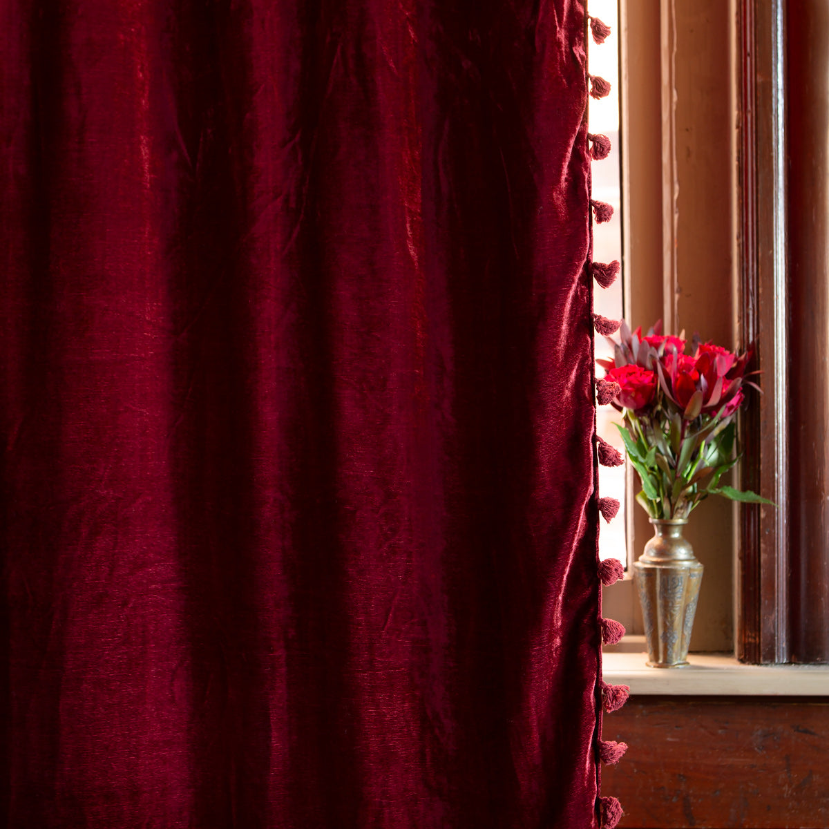 A crushed-velvet Ruby red curtain with tasseled edges, hanging on a rod pocket