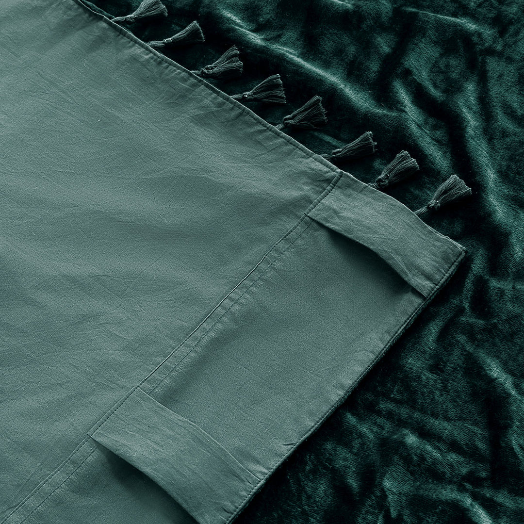 Green velvet tasseled curtain with a cotton backing. The corner of the curtain is folded over to show the backing. 