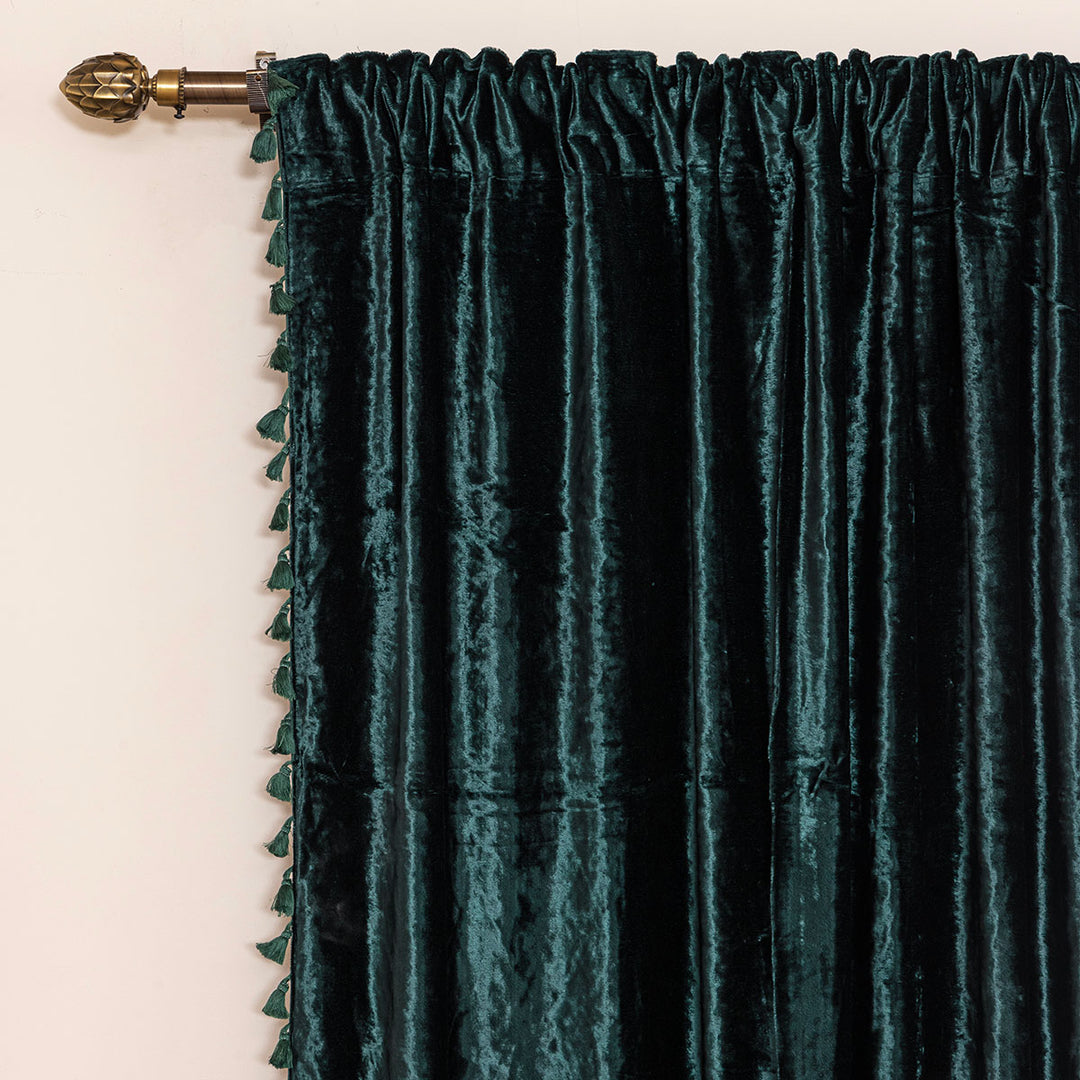 Dark green velvet curtain with tassels on a decorative rod on a beige wall.