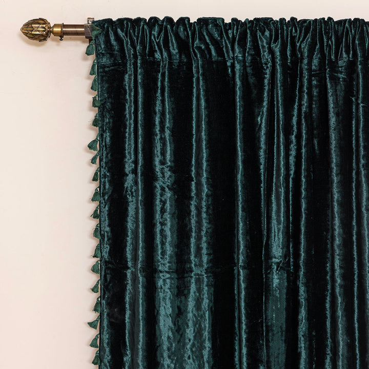Dark green velvet curtain with tassels on a decorative rod on a beige wall.