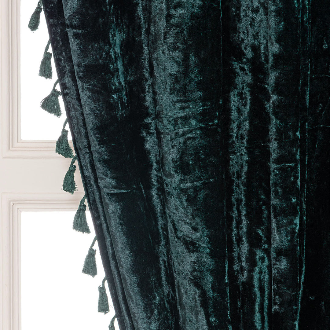 Dark green velvet curtain with tassels against a window.