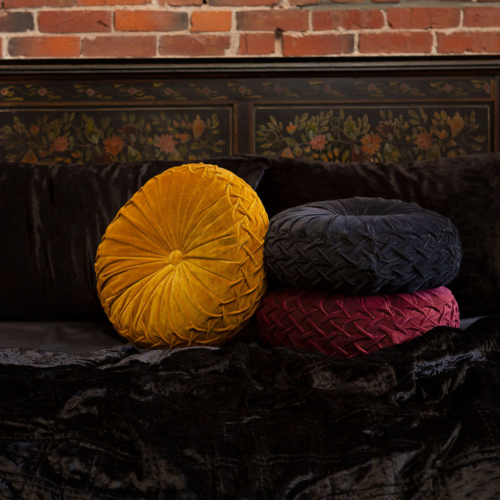 A pile of three velvet pintuck pillows in black, gold, and ruby red. Luxurious throw pillows by Sin in Linen on a bed of black velvet bedding. 